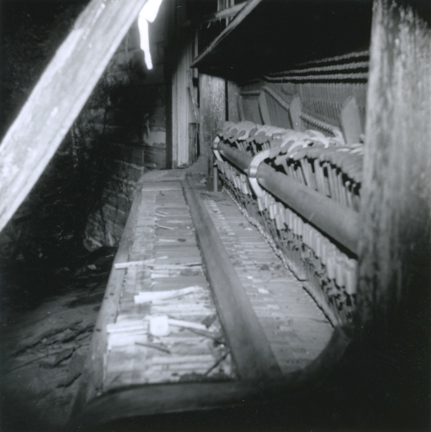 Black and white film print of an abandoned upright piano that has been mostly destroyed with heavy vignetting from the plastic lens of the camera